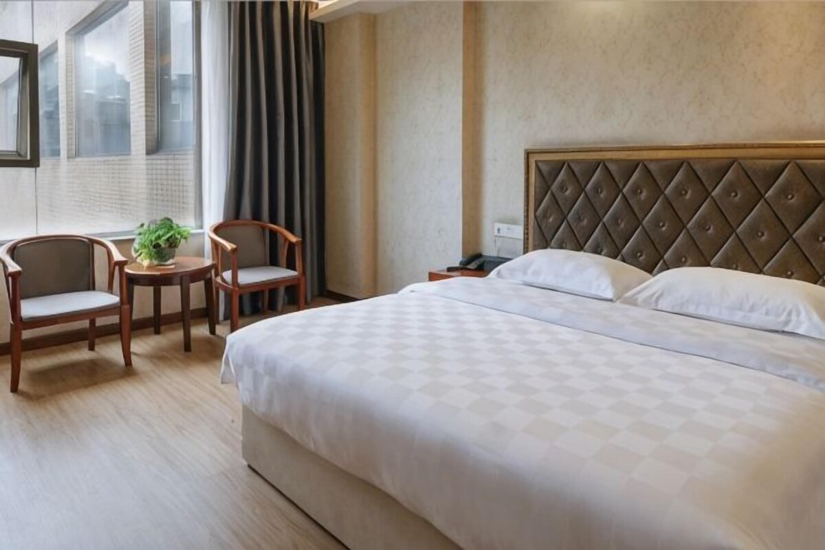 Una habitación de hotel con una cama grande, dos sillas, una mesita y una planta en maceta.