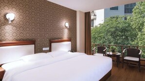 Habitación de hotel con una cama grande, dos mesitas de noche, un balcón con sillas y una pared con diseño.