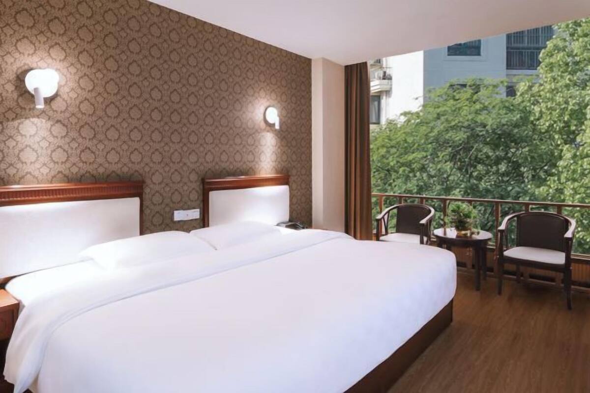 Ein Hotelzimmer mit einem großen Bett, zwei Nachttischen, einem Balkon mit Sitzgelegenheiten und einer Wand mit Musterung.