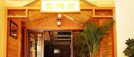 A hotel entrance with a sign above the door, wooden paneling, and a potted plant to the right.