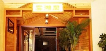 Entrada de hotel con un letrero sobre la puerta, paneles de madera y una planta en maceta a la derecha.