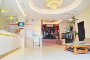 A hotel lobby with a reception desk, a staircase, and a dining area.