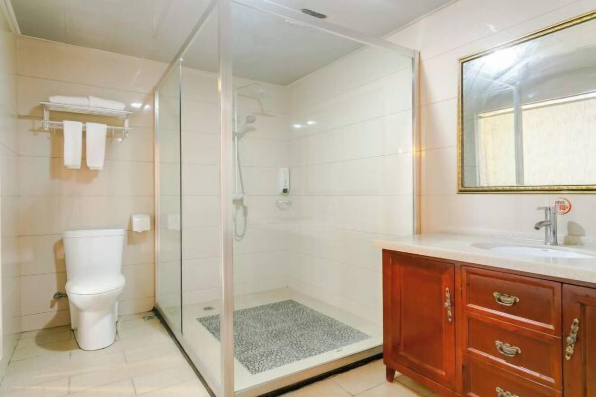 Ein Badezimmer mit einer Duschkabine, einer weißen Toilette und einem hölzernen Waschtisch mit Spiegel.