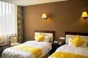 Habitación de hotel con dos camas, cada una con cabecero y almohada. Hay dos mesitas de noche con lámparas.
