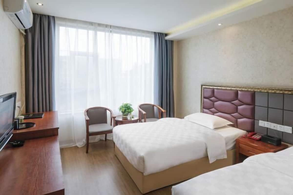 Ein Hotelzimmer mit zwei Betten, einem Fernseher, einem Schreibtisch und einem Sessel.