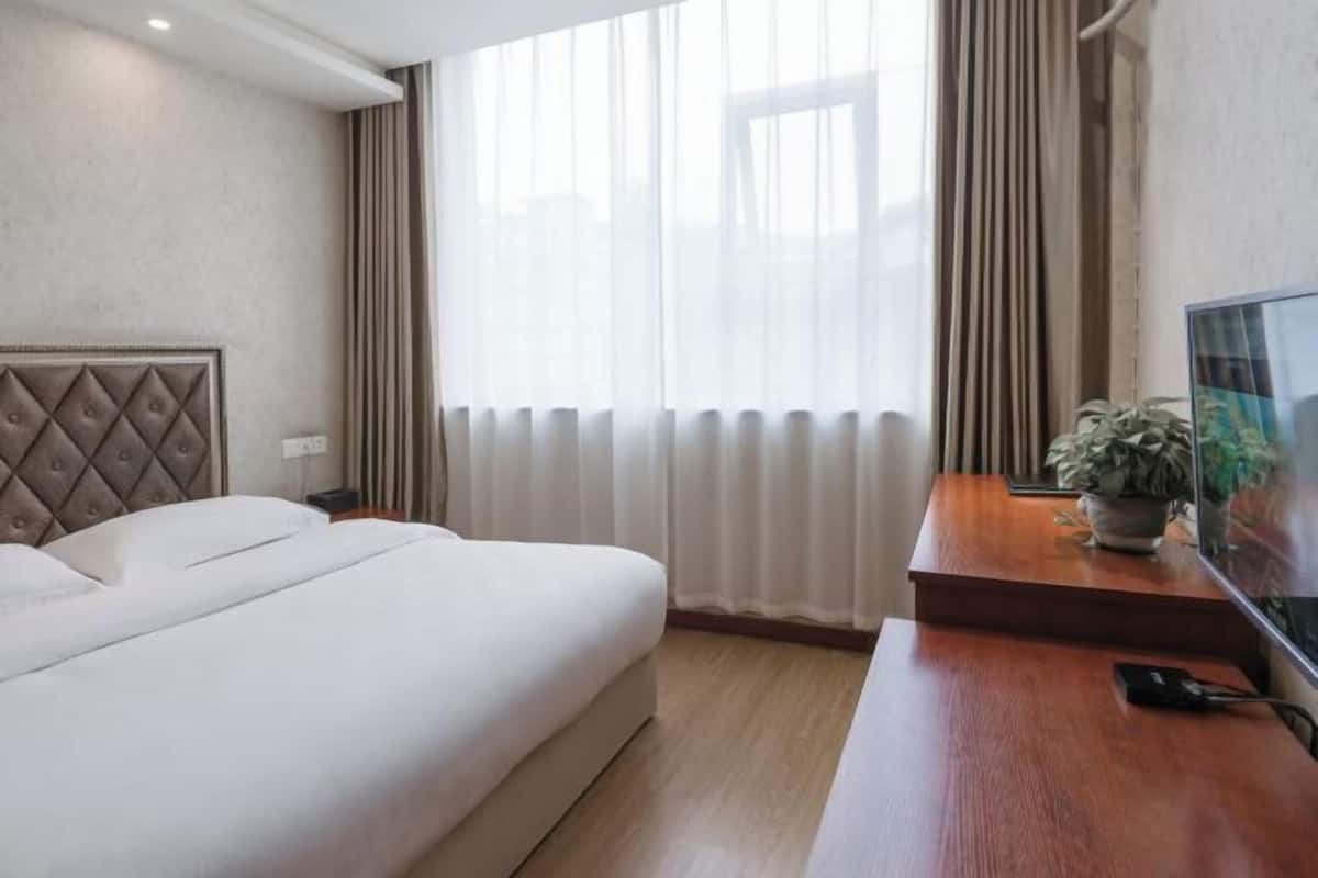 Ein Hotelzimmer mit einem Bett, einem Holztisch, einem Fernseher und einem Fenster mit Vorhängen.