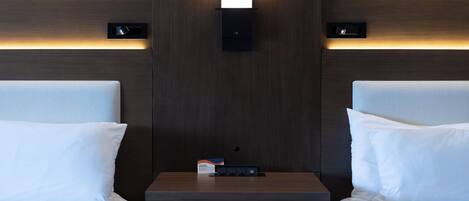Habitación de hotel con dos camas, una mesita de noche y un aplique de pared.