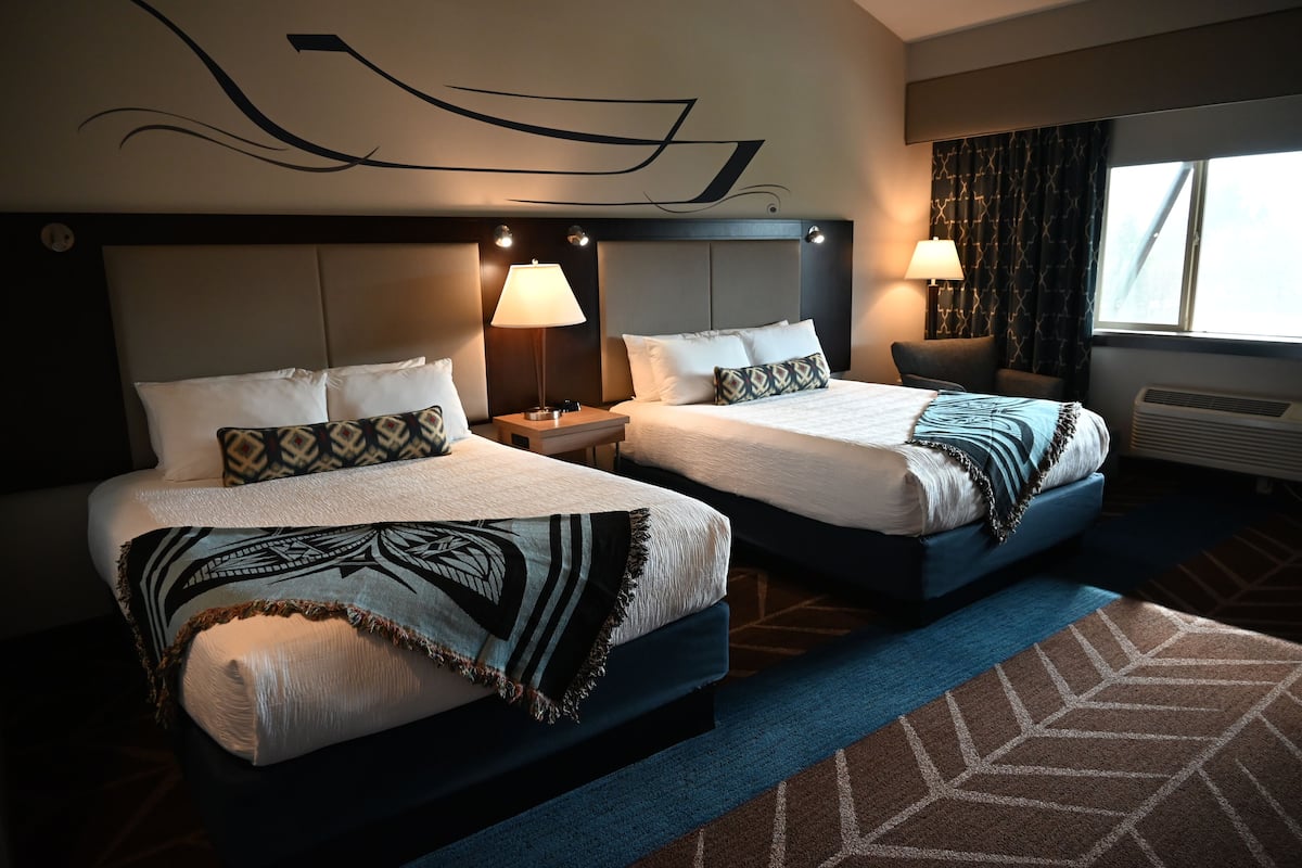 A hotel room with two beds, each with a headboard, bedside lamps, and a patterned throw blanket.