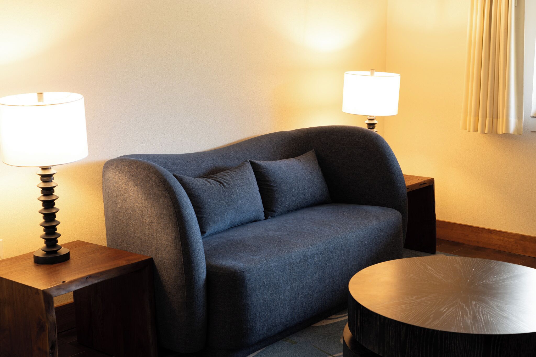 Une chambre moderne avec un canapé bleu foncé, deux tables de chevet avec des lampes et une table basse ronde.