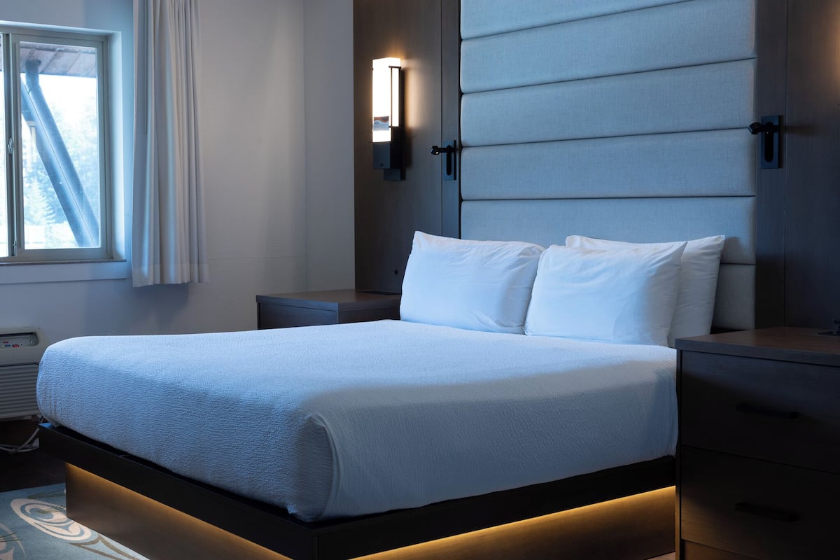 A modern hotel room with a large bed, bedside tables, a wall-mounted light, and a window with curtains.