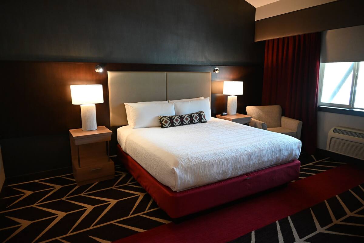 A hotel room with a large bed, two bedside lamps, a chair, and a window with curtains.