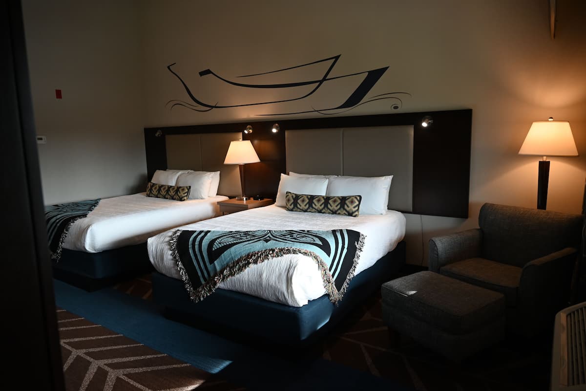 A hotel room with two beds, a sofa, a chair, and a decorative wall design.