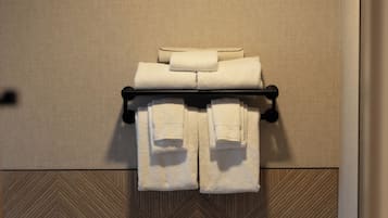 A bathroom with a toilet, a towel rack with folded towels, and a trash bin.
