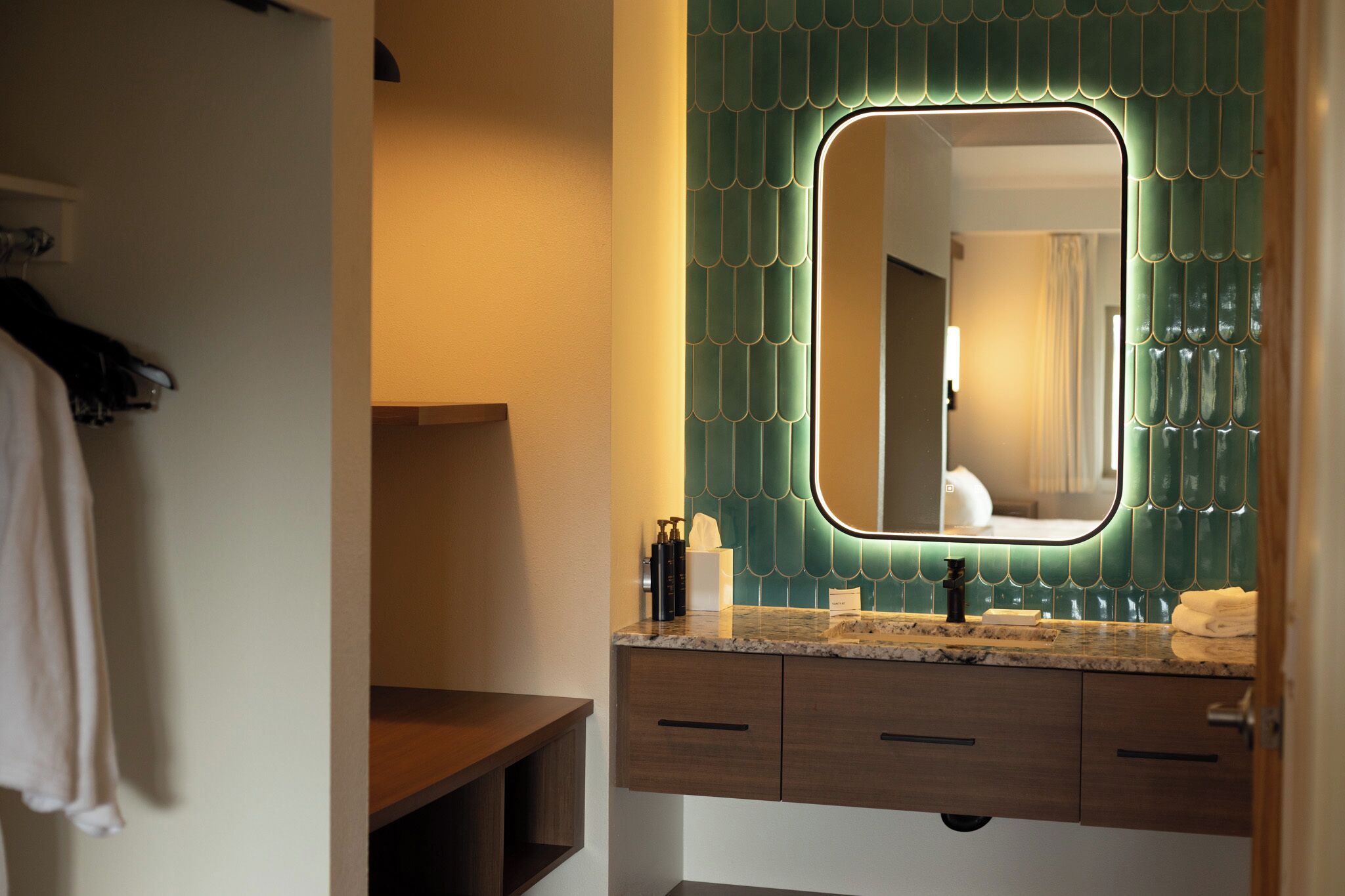 A bathroom with a vanity, a mirror, and a green tiled backsplash.