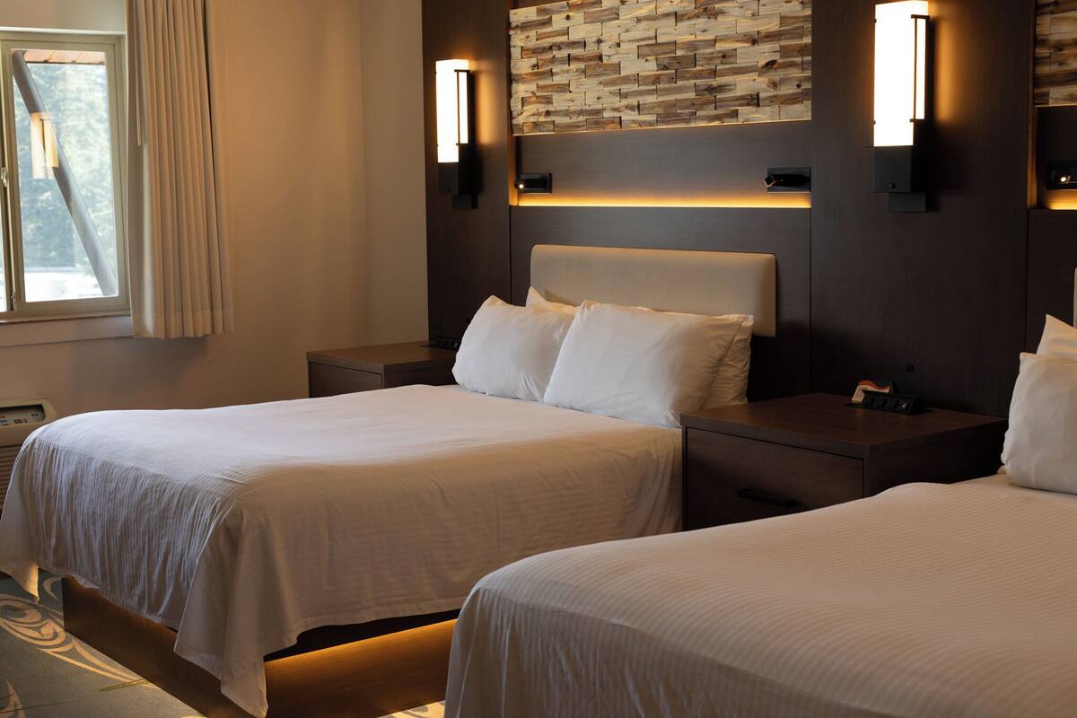 A hotel room with two beds, a wooden accent wall, and bedside lamps.