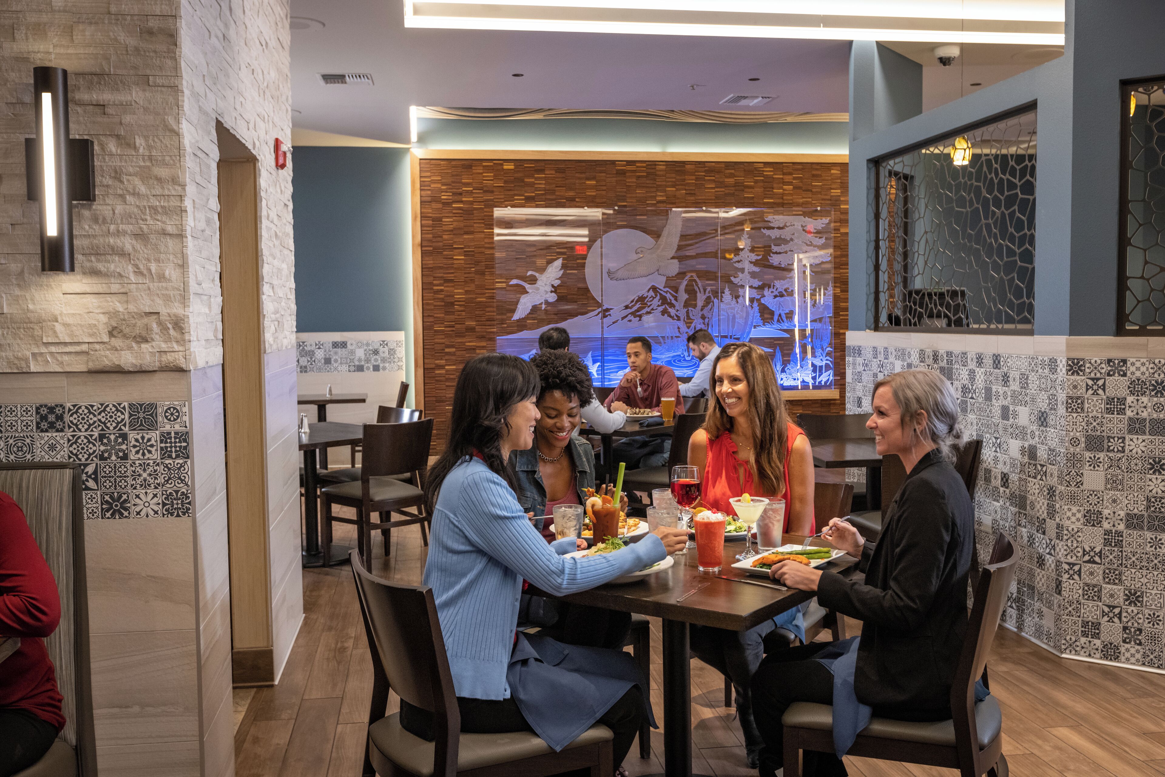 A restaurant with a modern interior, featuring a mix of stone and tile walls, and a large mural on the back wall.