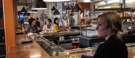 Un interior de restaurante con barra, mesas de comedor y lámparas colgantes.