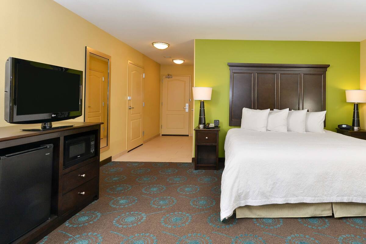 A hotel room with a bed, a television, a microwave, a nightstand, and a lamp.