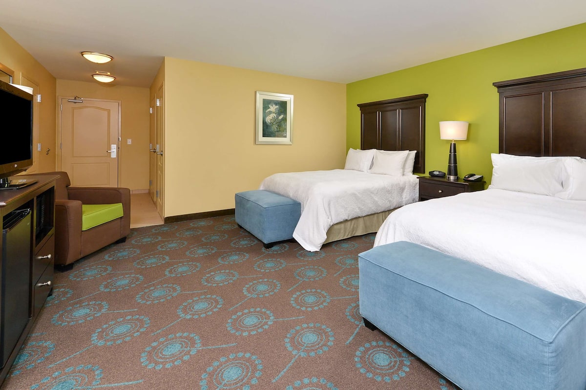 A hotel room with two beds, a TV, a desk, and a chair.