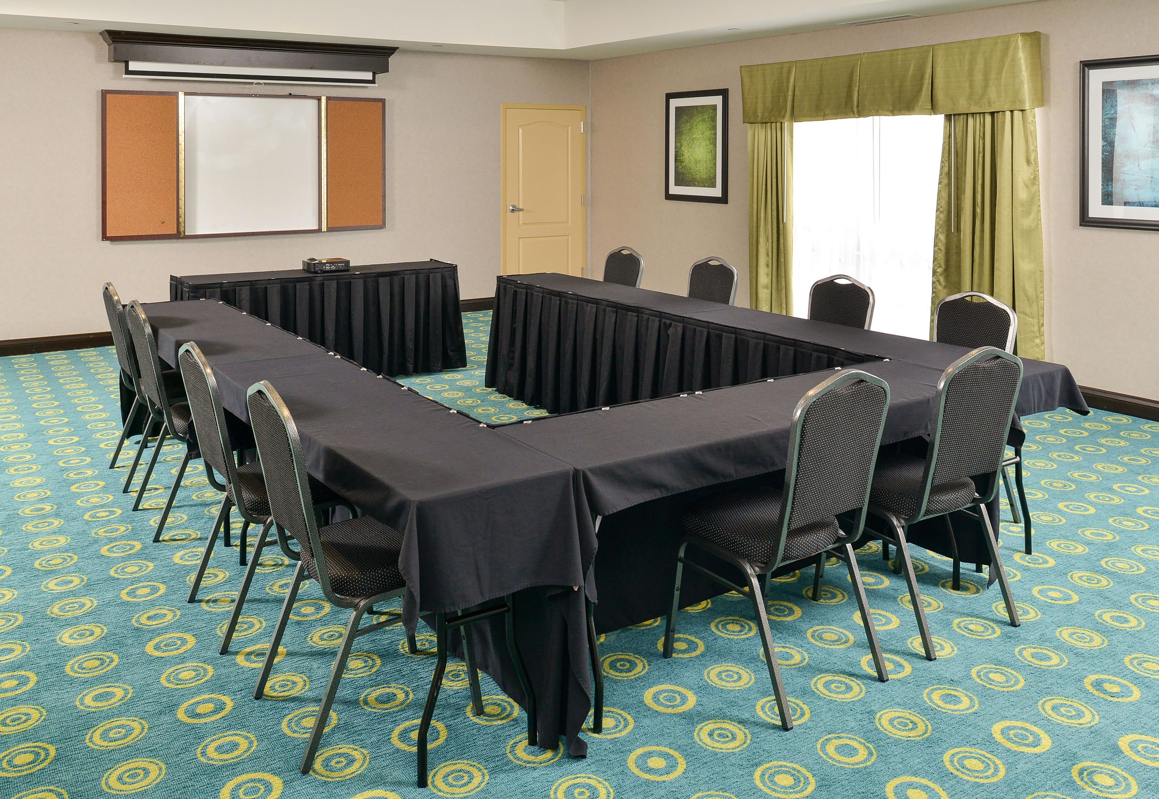 A conference room with a long table, chairs, a projector screen, and a door.