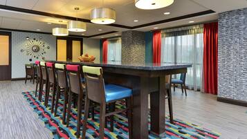Ein Hotelzimmer mit einer langen Bar, mehreren Stühlen, einem gemusterten Teppich und einer Wanddekoration.