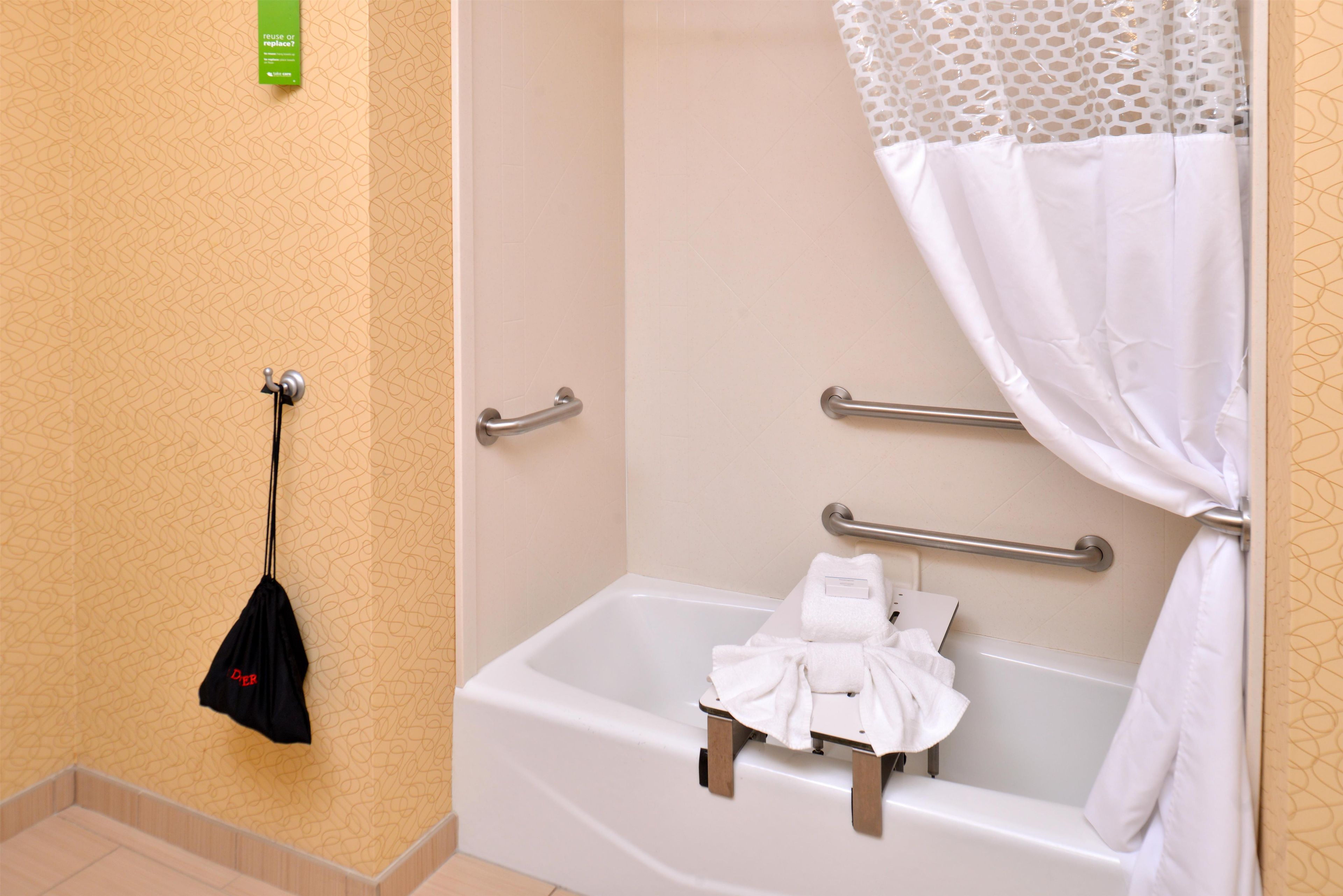 Un baño con bañera, barras de apoyo, toallero y cortina de ducha.