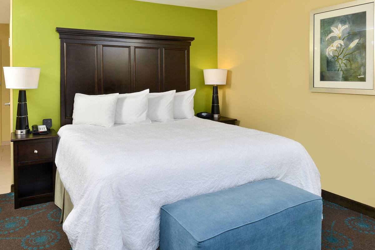 A neatly made bed with white linens, a dark wooden headboard, and a blue bench at the foot of the bed.