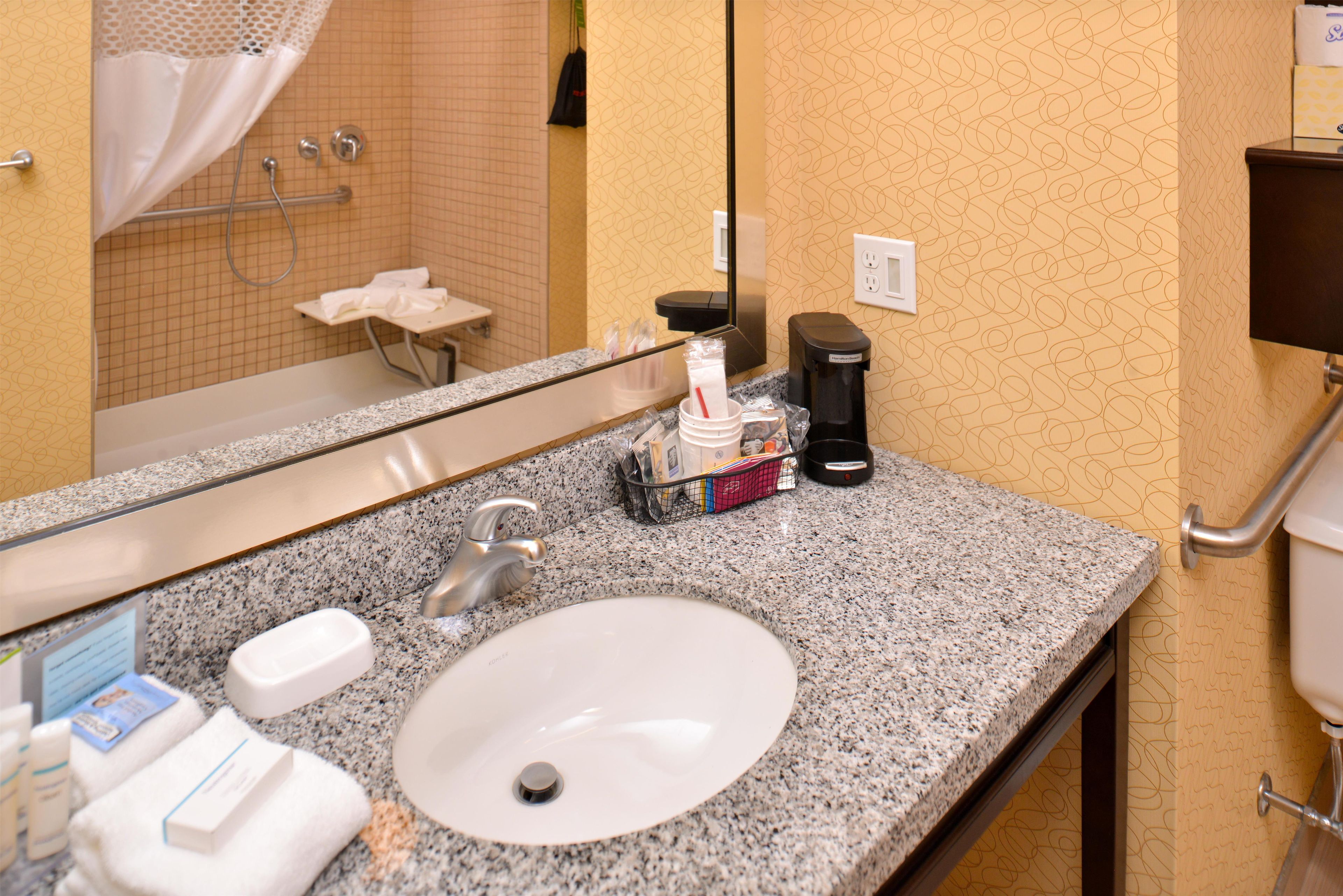 Ein Hotelbad mit einer Arbeitsplatte aus Granit, einem Waschbecken, einem Spiegel und einem Handtuchhalter.
