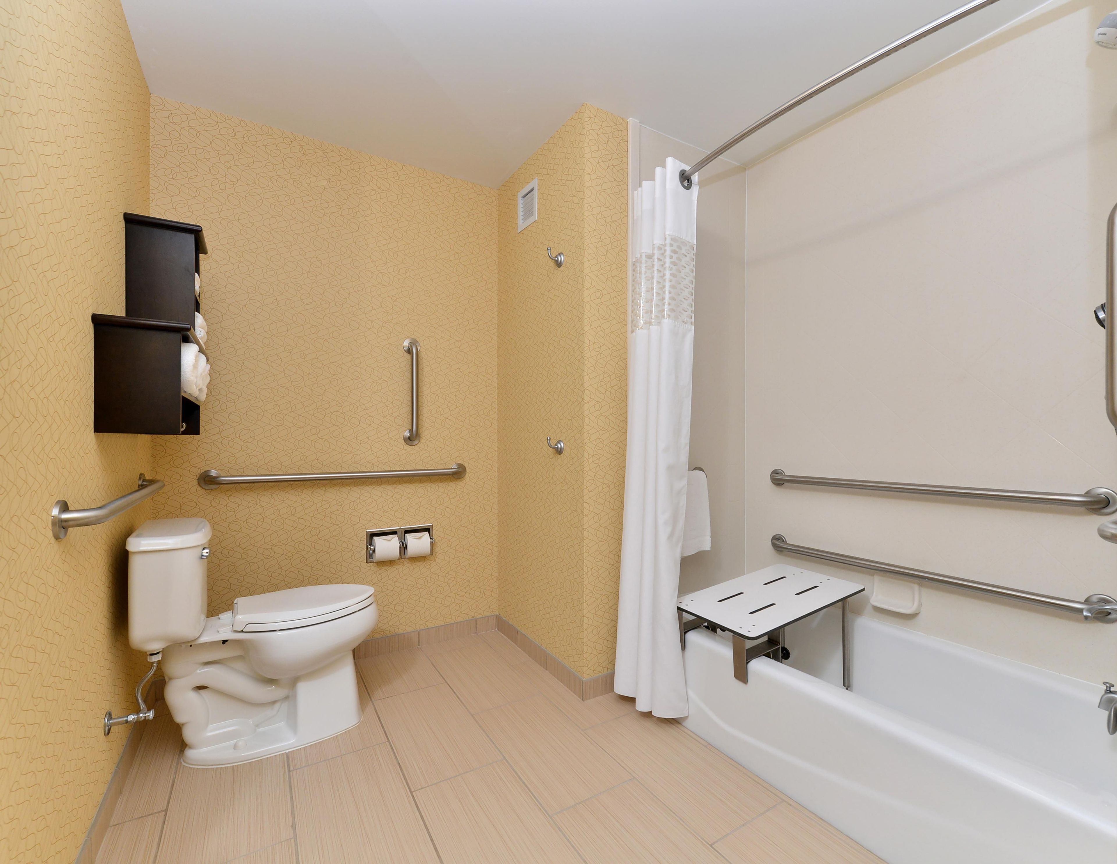 Un baño con inodoro, bidé y bañera. Incluye barras de apoyo y cortina de ducha.