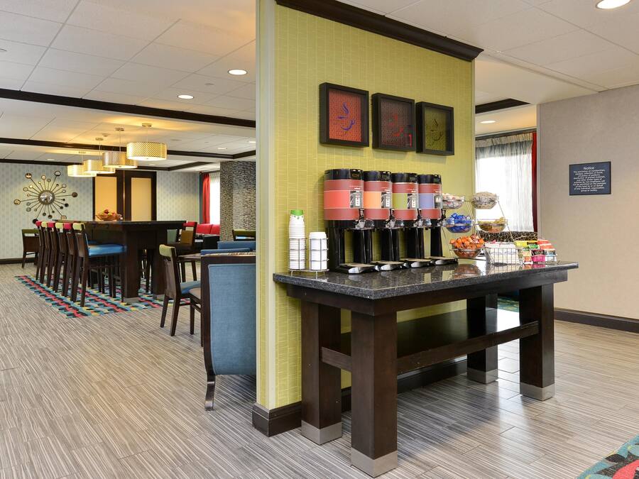 Un vestíbulo de hotel con una estación de café, zona de estar y una pared decorada con obras enmarcadas.