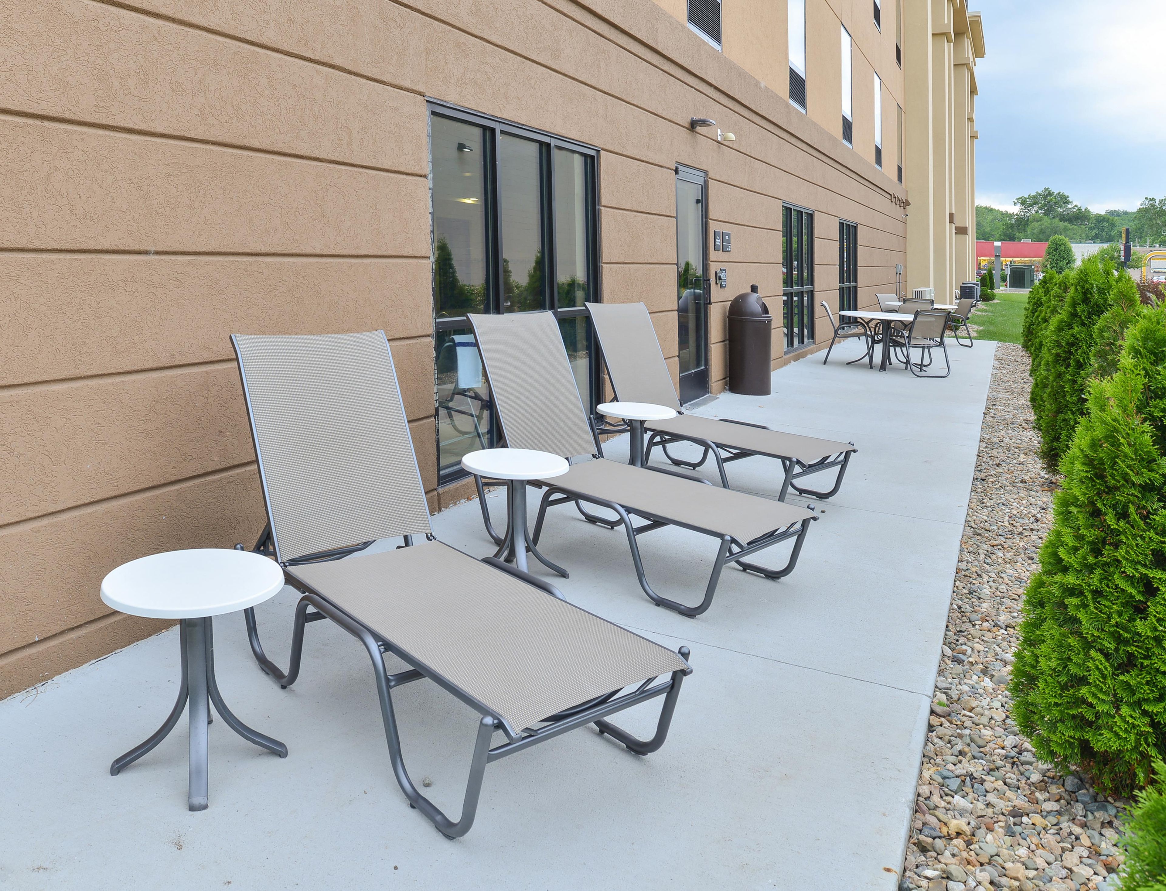 Outdoor seating with tables and chairs, a building with windows, and a hedge.