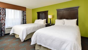 A hotel room with two beds, a window with curtains, a bedside table with a lamp, and a carpet with a geometric pattern.