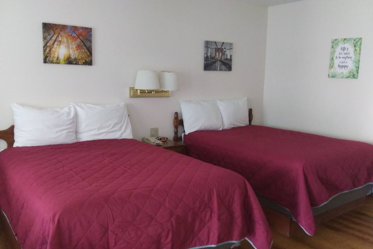 A hotel room with two beds, white bedding, a nightstand with a lamp, and wall art.