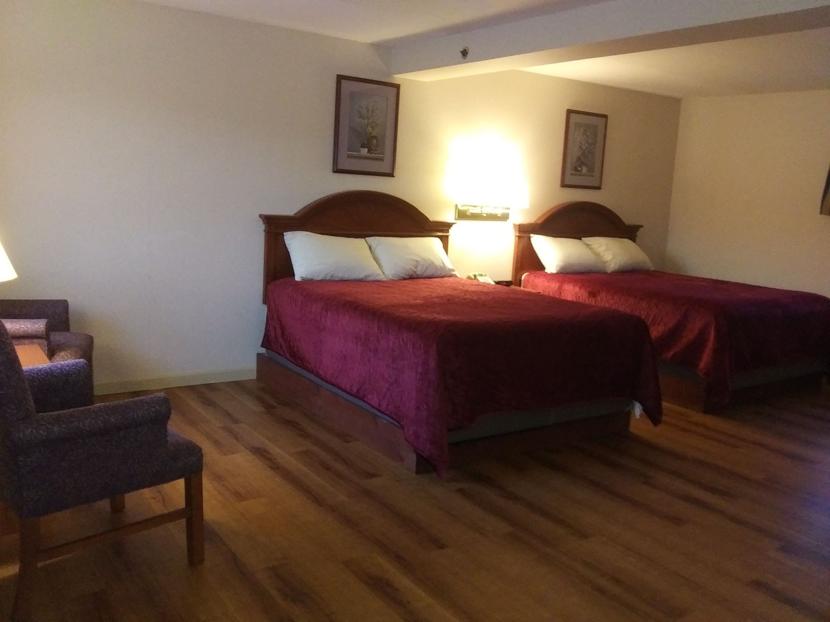 A hotel room with two beds, wooden flooring, a chair, and two wall-mounted lamps.