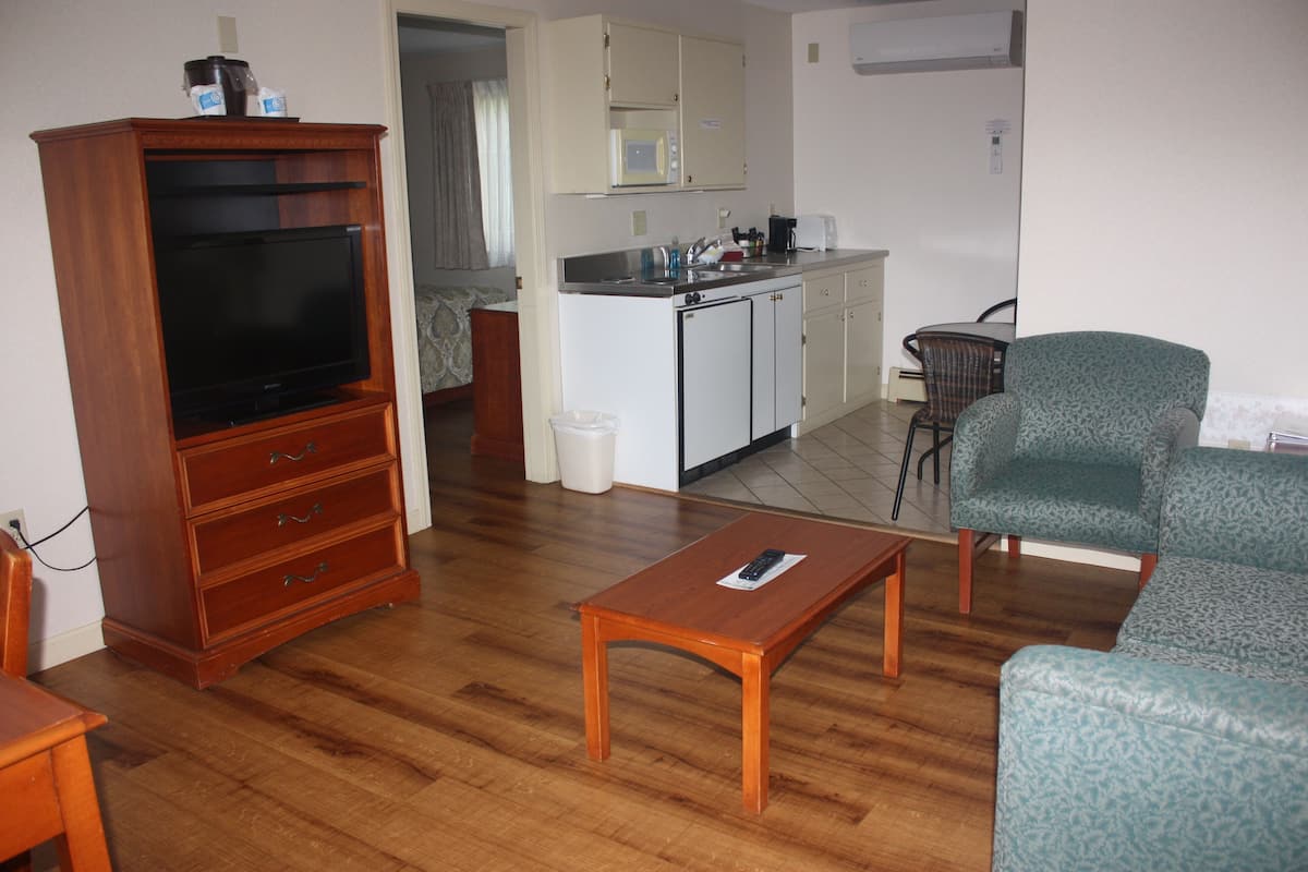 A living room with a TV, wooden furniture, a coffee table, and a patterned armchair.
