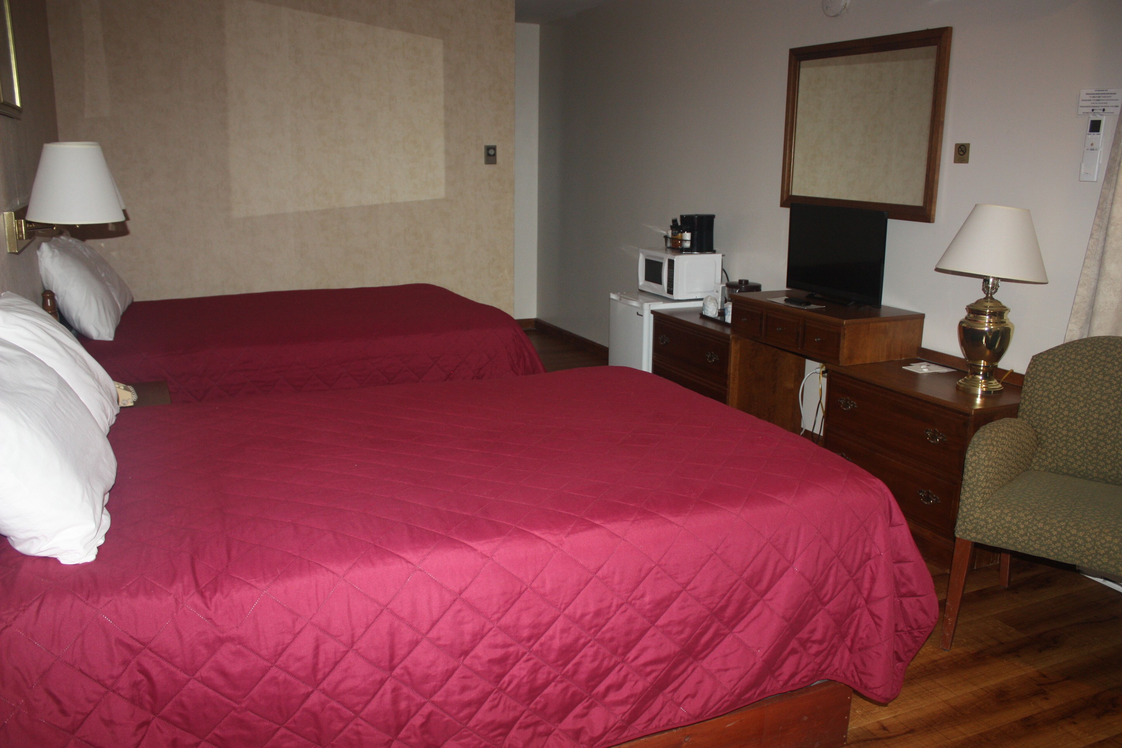 Una habitación de hotel con dos camas, un tocador, televisión, microondas y una silla.