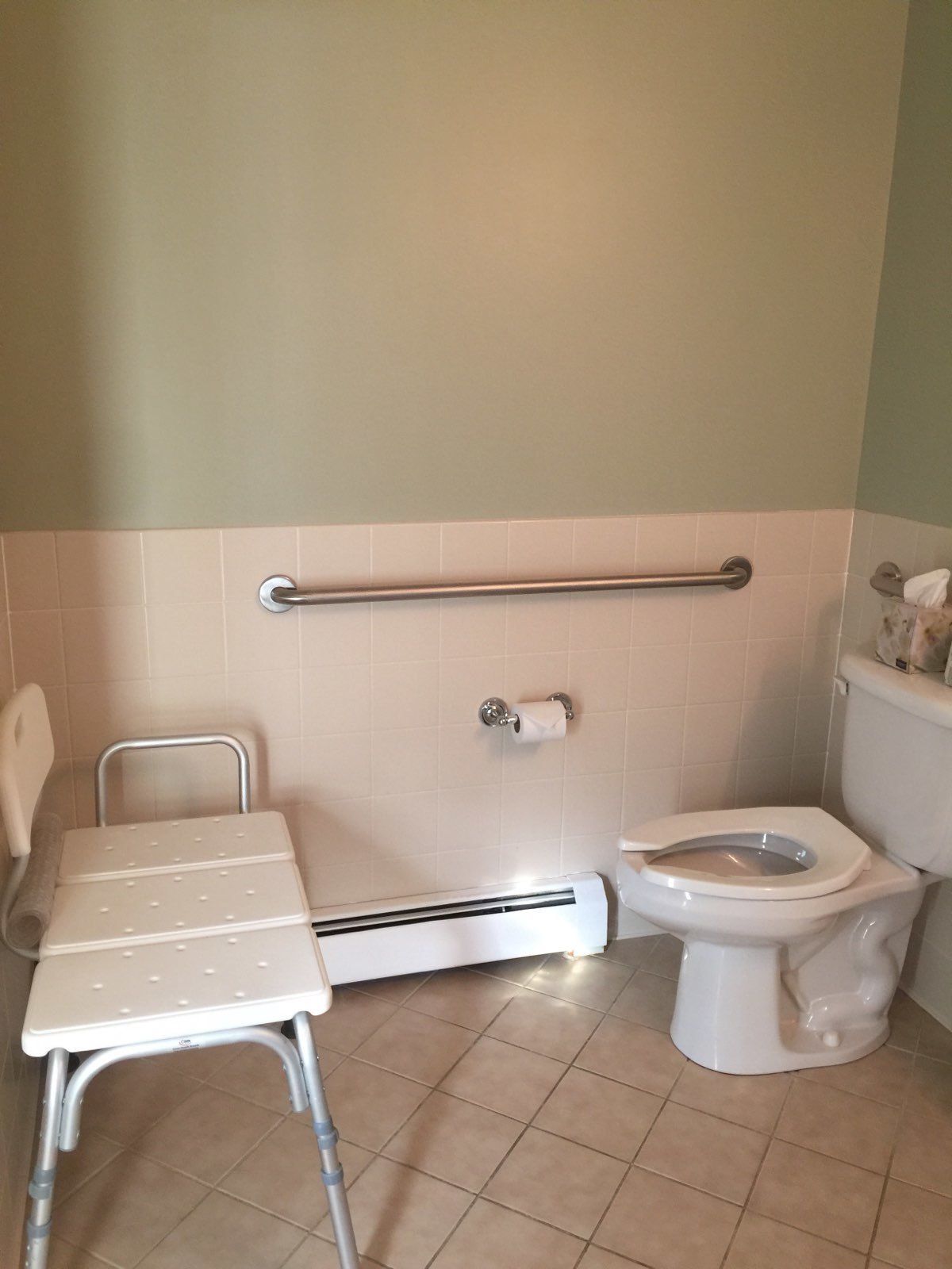 Un baño con banca accesible para sillas de ruedas, un inodoro y una barandilla.