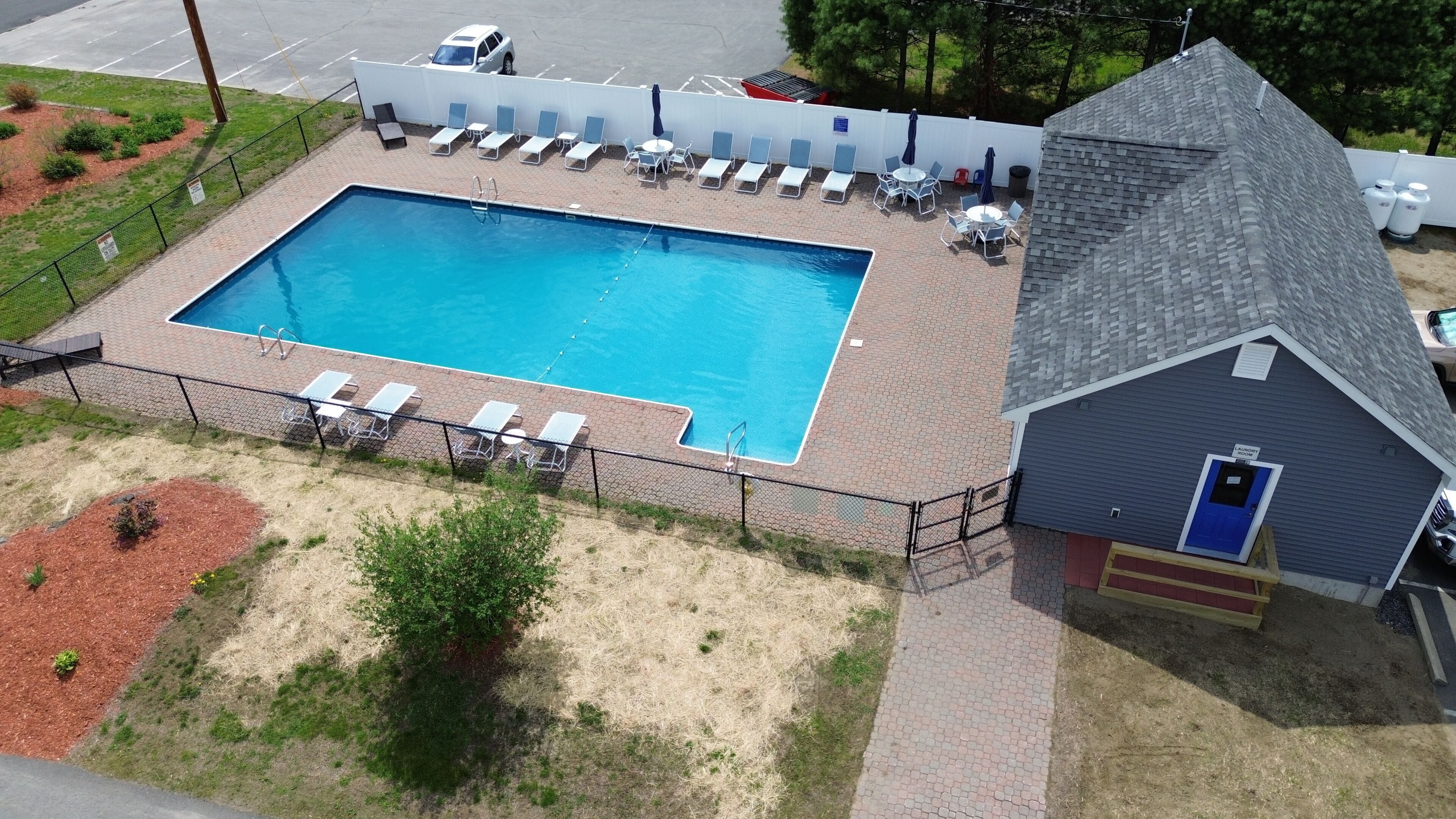 En rektangulär swimmingpool med ett inhägnat poolområde, solstolar och en liten byggnad med en blå dörr.