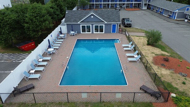 A rectangular swimming pool with a brick deck, surrounded by lounge chairs and umbrellas, with a building in the background. - The Towne Motel (Skowhegan)