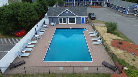 A rectangular swimming pool with a brick deck, surrounded by lounge chairs and umbrellas, with a building in the background.