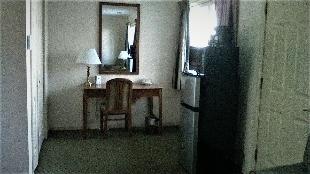 A small room with a desk, chair, and a refrigerator.