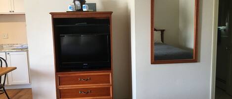 A room with a wooden entertainment center, a mirror, and a bed.