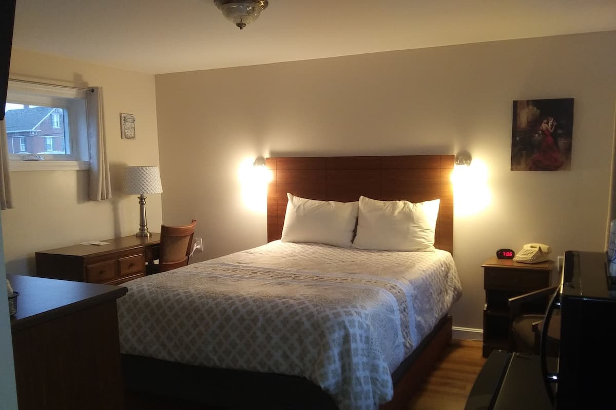 A hotel room with a bed, bedside table, lamp, and a clock on the nightstand.