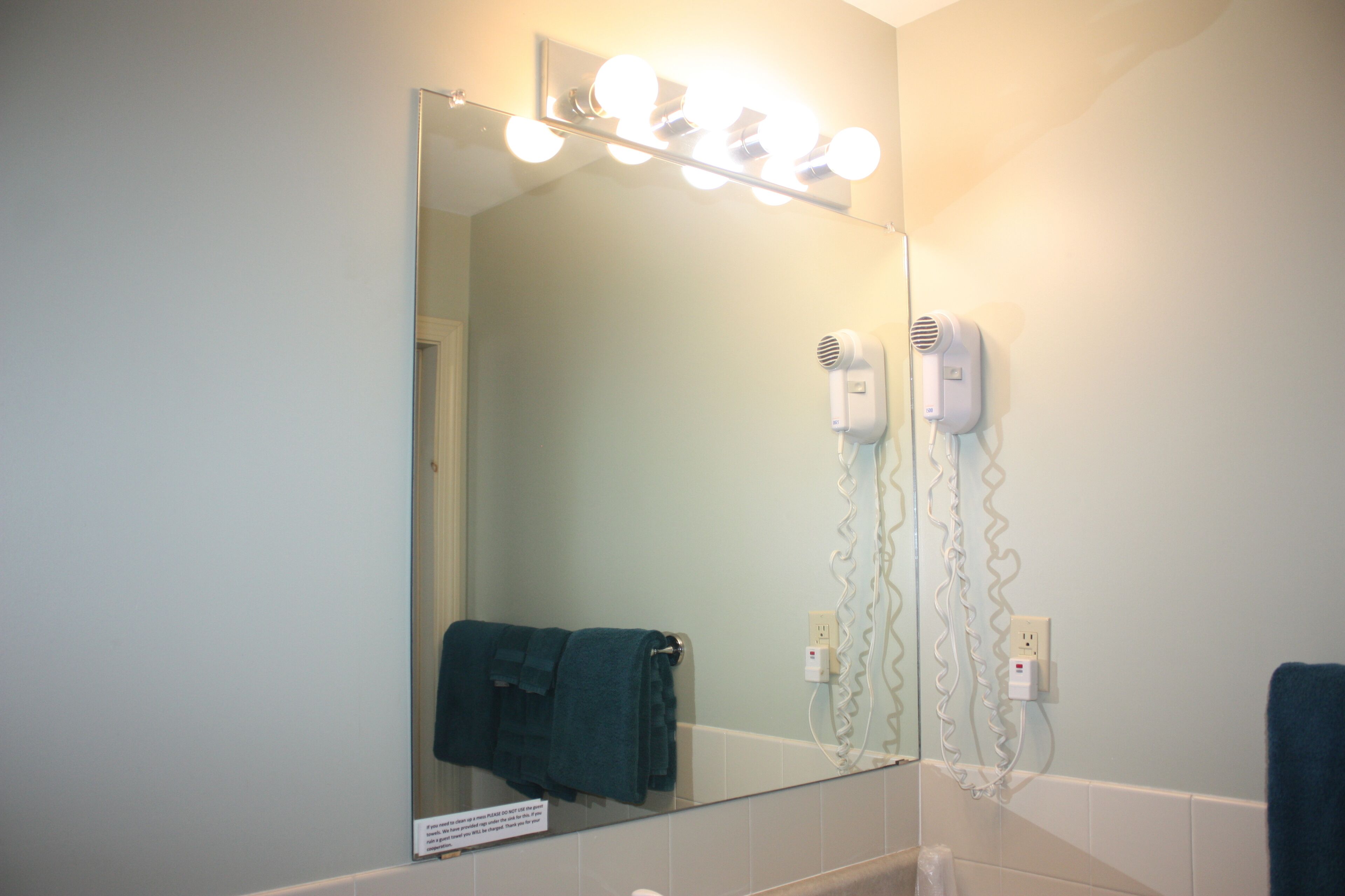 A bathroom with a mirror, lights, a towel rack, and a hairdryer.