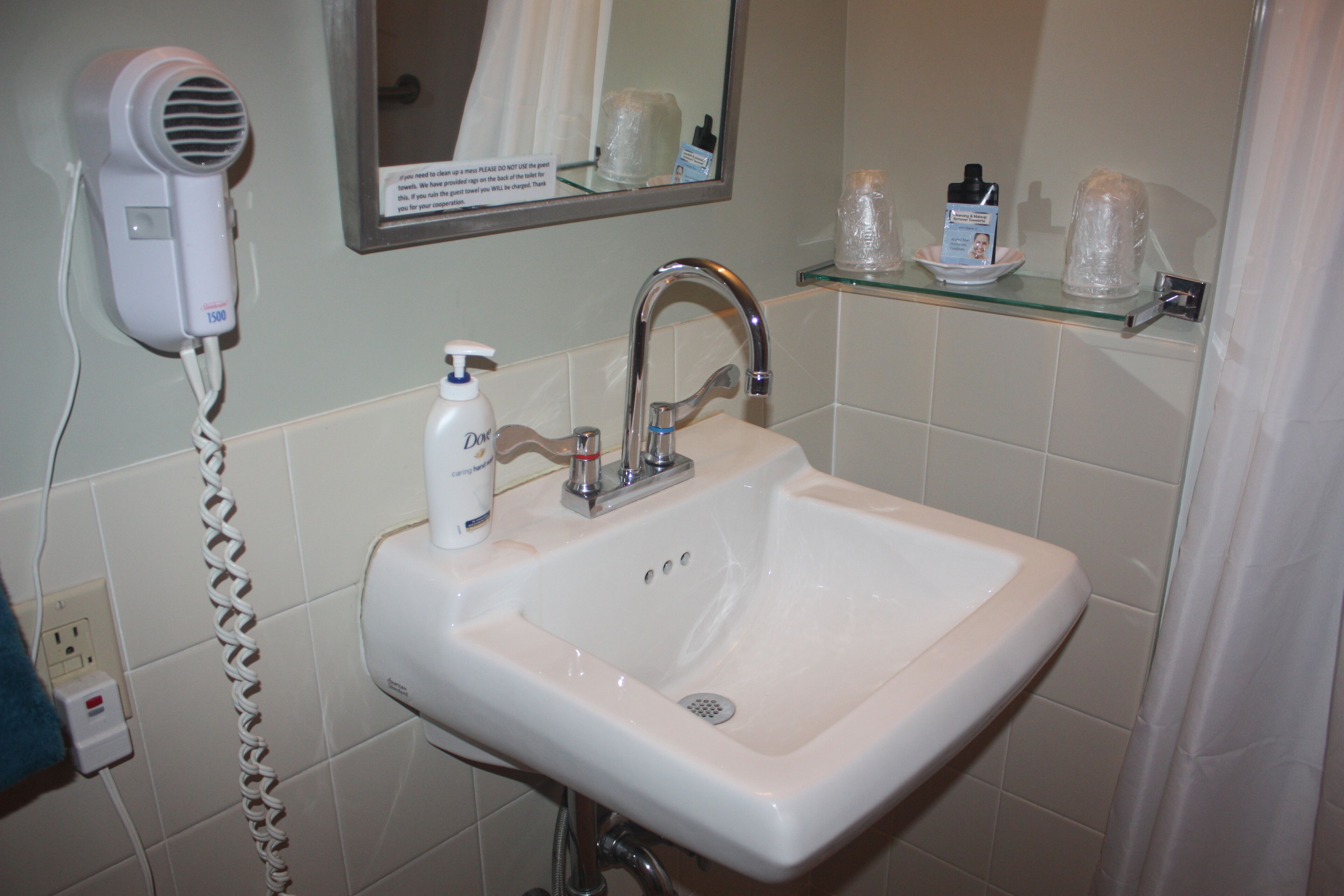 A bathroom with a white sink, a hairdryer, and a mirror.