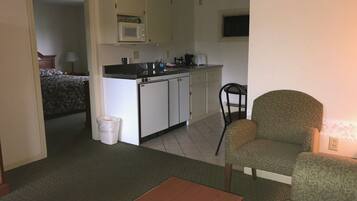A compact room with a kitchenette, a single bed, a small table, and a chair.