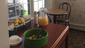 A breakfast setup with a fruit basket, a pitcher of orange juice, and a bowl of cereal on a wooden table. - The Towne Motel (Skowhegan)
