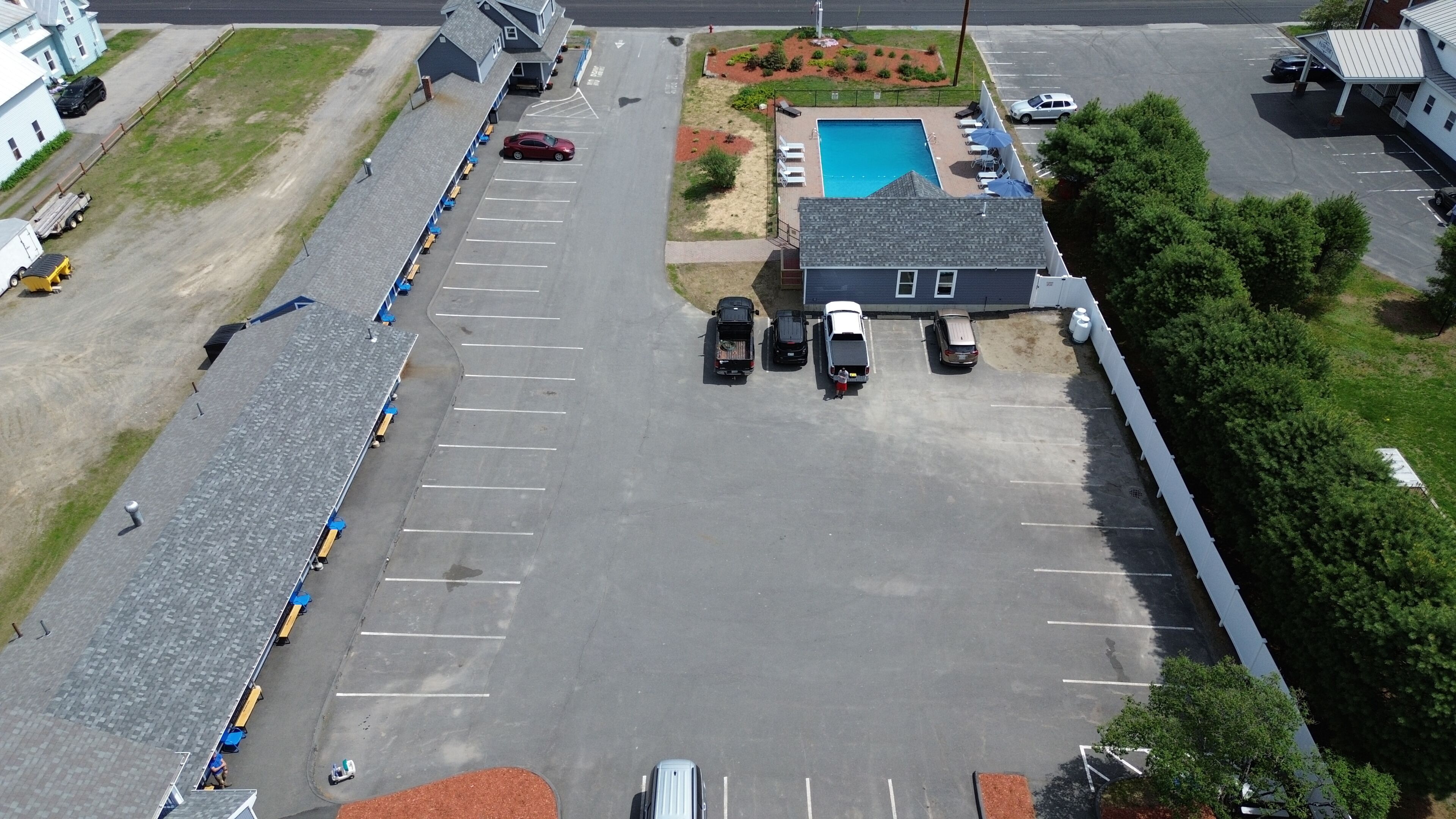 Vista aérea de un estacionamiento con piscina, un área techada con sillas de descanso y un edificio de techo inclinado.