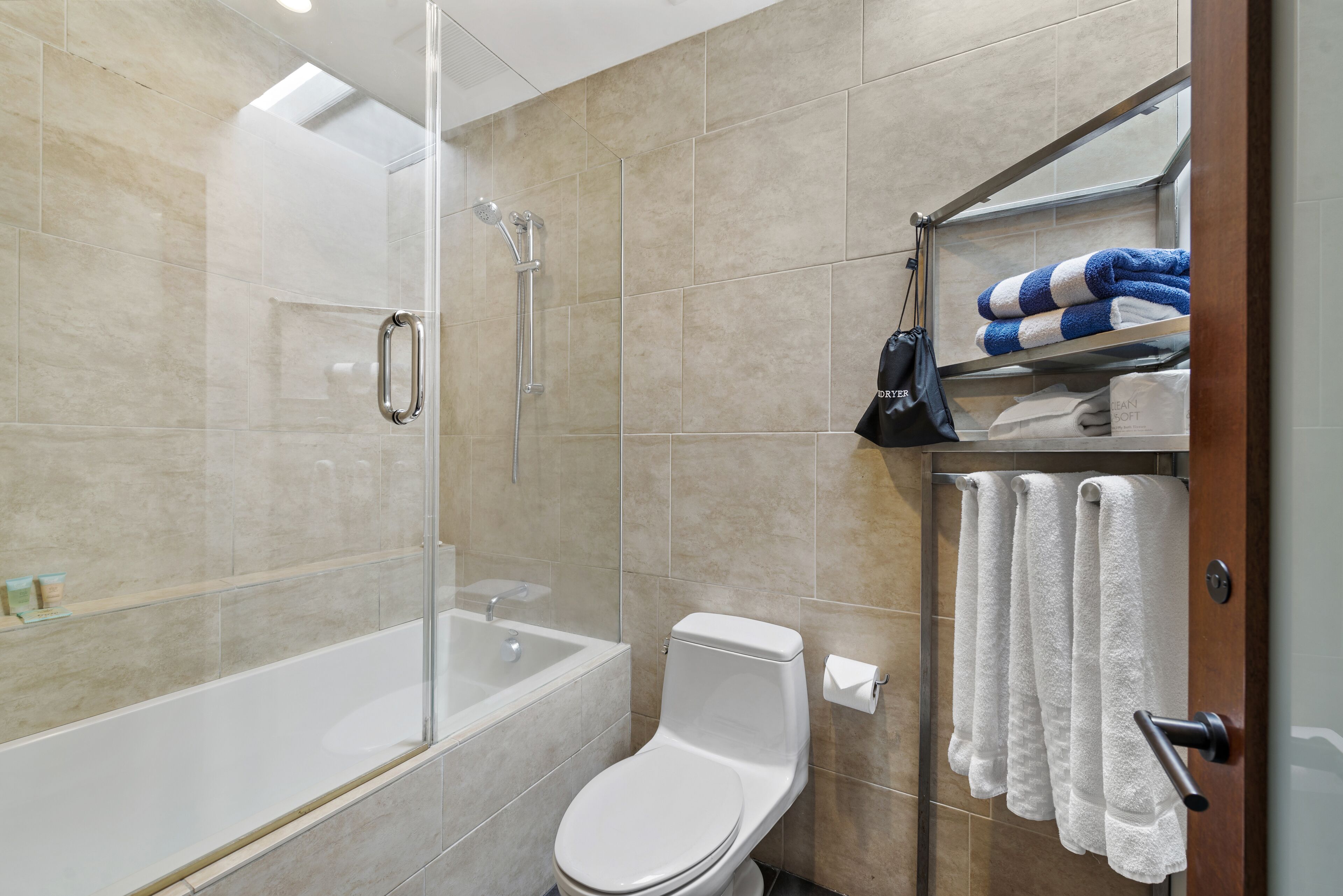 A modern bathroom with a glass-enclosed shower, a white toilet, and a shelf with towels and toiletries.