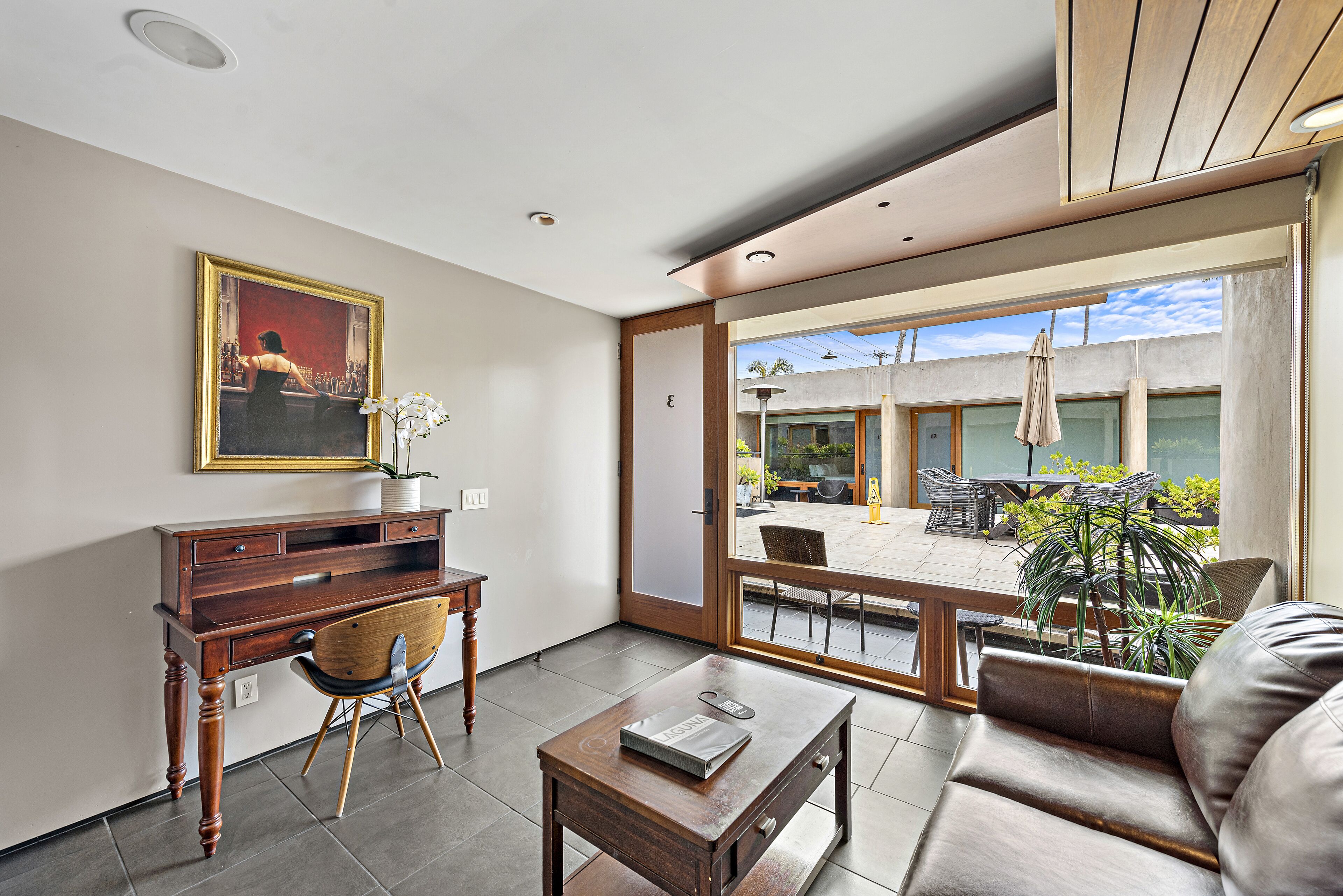 Un salón moderno con un escritorio de madera, un sofá cómodo y un amplio ventanal con vistas al patio exterior.